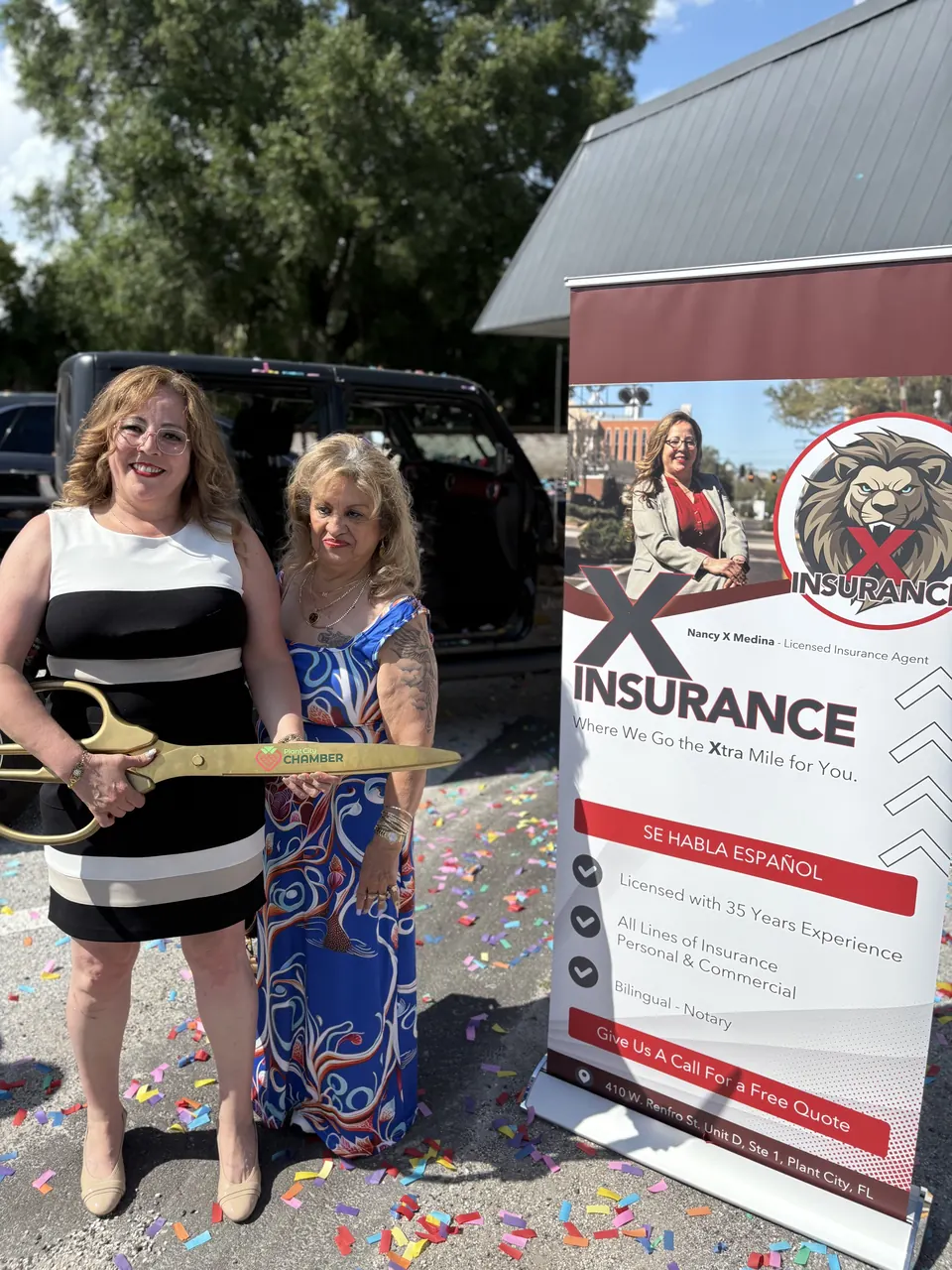 Nancy with the Chamber ribbon-cutting scissors beside an X Insurance banner