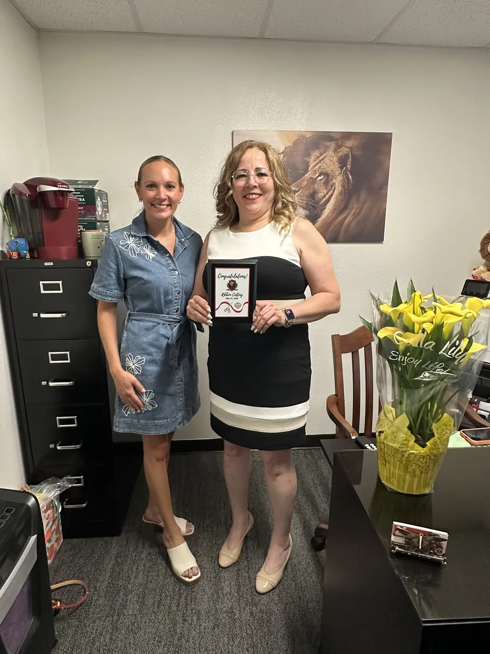 Nancy in her office holding a ribbon-cutting congratulations plaque