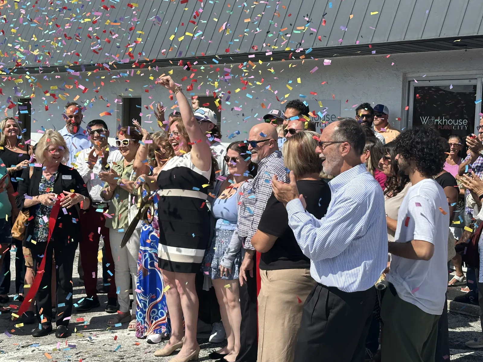 Nancy cutting the ribbon with neighbors and local business leaders as confetti falls